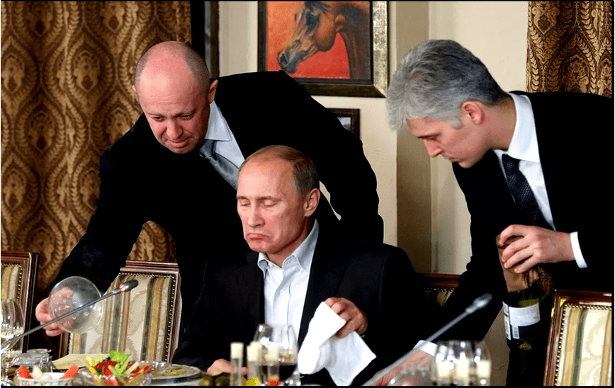 A photo from November 2011 shows Yevgeny Prigozhin (L) helping Vladimir Putin at a banquet near Moscow